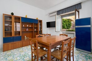 Ein Essbereich mit Holztisch und -stühlen, einer blauen Kommode mit Glastüren und einem Fenster mit Blick auf Grünflächen.