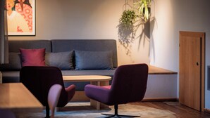 Una sala de estar moderna con un sofá, dos sillones, una mesa de centro de madera y una planta colgante.