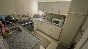 A compact kitchen with white cabinets, a granite countertop, a stove, a microwave, and a sink. - Stylish Downtown Cairo Apartment with Balcony View & Prime Location (Cairo)