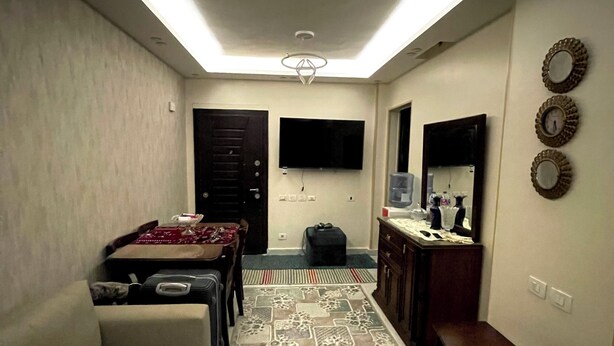 A living room with a sofa, a coffee table, a TV, a patterned rug, and a bench. - Stylish Downtown Cairo Apartment with Balcony View & Prime Location (Cairo)