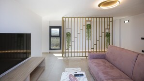 Ein modernes Wohnzimmer mit Flachbildfernseher, einer Couch, einem Couchtisch und einer dekorativen Raumtrennung mit Pflanzen.