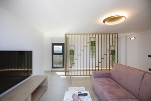 Ein modernes Wohnzimmer mit Flachbildfernseher, einer Couch, einem Couchtisch und einer dekorativen Raumtrennung mit Pflanzen.