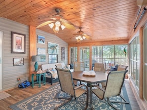 A wooden interior with a ceiling fan, a dining table with chairs, and artwork on the walls.