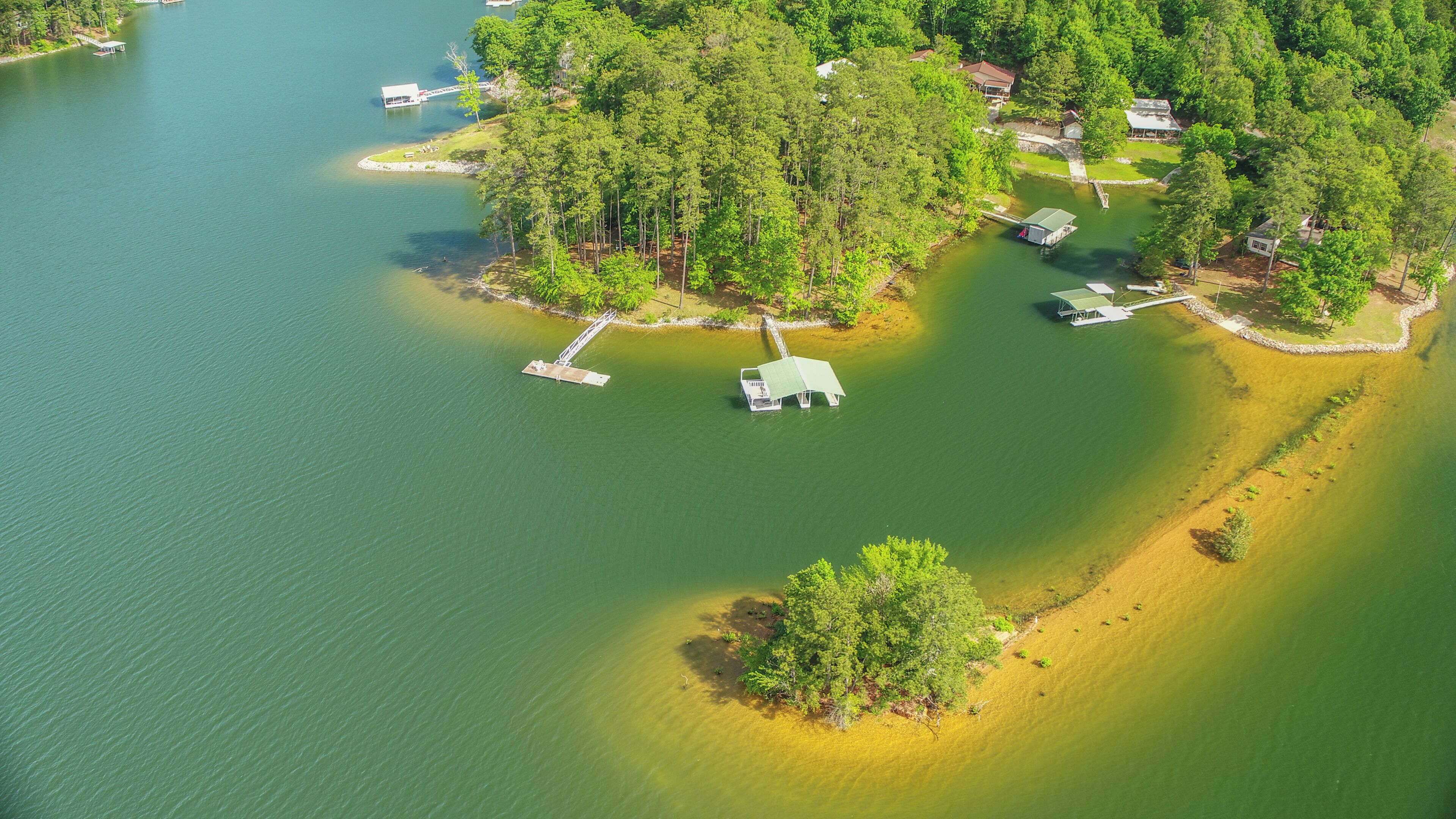 Eine Luftaufnahme eines Sees mit einer Uferanlage, einer kleinen Insel und einem Haus, das von dichtem Baumbestand umgeben ist.