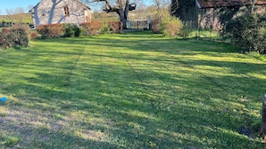 A stone building with a sloped roof, surrounded by a well-maintained lawn and various shrubs. - Le vieux noyer - Room Two - In the heart of the Morvan countryside. (Montlay-en-Auxois)