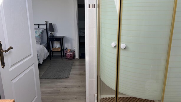 A room with a bed, a bedside table with a lamp, a small table with a tissue box, and a shower area with frosted glass doors. - Le vieux noyer - Room Two - In the heart of the Morvan countryside. (Montlay-en-Auxois)