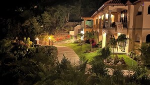 A well-lit, multi-story building with a landscaped garden, a paved driveway, and a view of the surrounding hills. - New 1-Bedroom villa with plunge pool on St John's amazing North Shore. (St John)