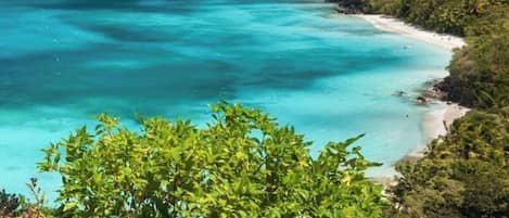 A coastal landscape with a beach, clear turquoise waters, and lush green hills.