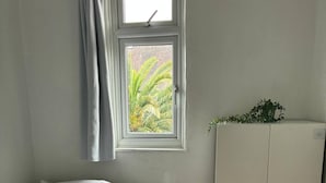 Ein Schlafzimmer mit Bett, Kleiderschrank, einem Fenster mit Vorhängen und Blick ins Grüne.