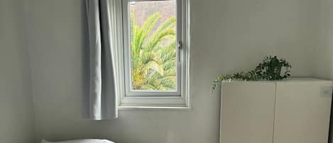 Un dormitorio con cama, armario, ventana con cortinas y vistas a zonas verdes.