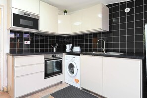 A modern kitchen with a built-in oven, microwave, and washing machine, a sink, and black tiled backsplash. - Full House 2 Bedrooms, 2 Bathrooms, Near Tube st (London)