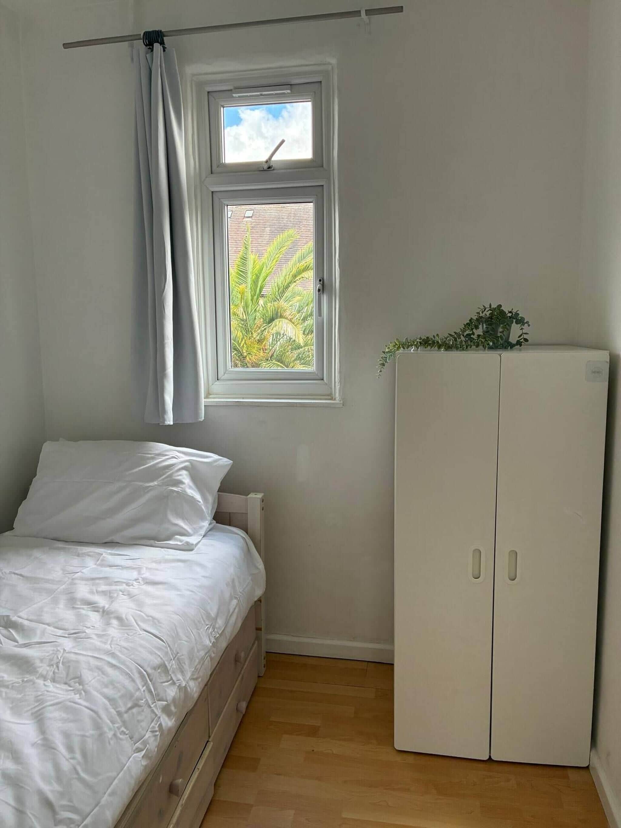 Une chambre à coucher avec un lit, une fenêtre avec des rideaux, un radiateur et une armoire.