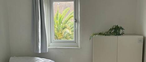 Une chambre à coucher avec un lit, une fenêtre avec des rideaux, un radiateur et une armoire.