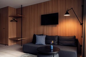 Una sala moderna con un sofá, un televisor de pantalla plana, una lámpara colgante y una pequeña mesa con un florero.