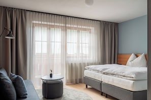 Un dormitorio con una cama, un sofá, una mesa redonda y cortinas traslúcidas.
