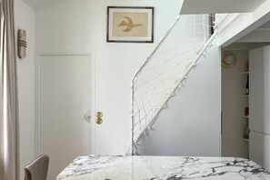 Ein Zimmer mit einem Marmortisch, einer weißen Tür, einem gerahmten Bild und einer weißen Treppe.