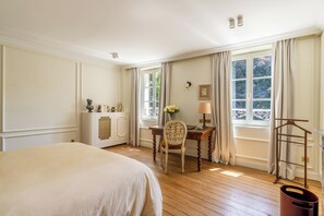 Ein Hotelzimmer mit einem großen Bett, einem Schreibtisch mit Stuhl, einem Fenster mit Vorhängen und einem an der Wand befestigten Kleiderhaken.