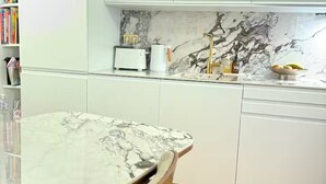 Una cocina con armarios blancos, encimera de mármol y grifo dorado.