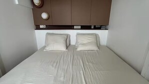 Una cama individual con colchón blanco y dos almohadas, cabecera de madera y una mesita de noche con lámpara.