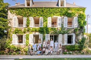 Ein Gebäude mit vielen Fenstern, einige davon mit Fensterläden, und eine Gruppe von Personen, die davor zusammenstehen.