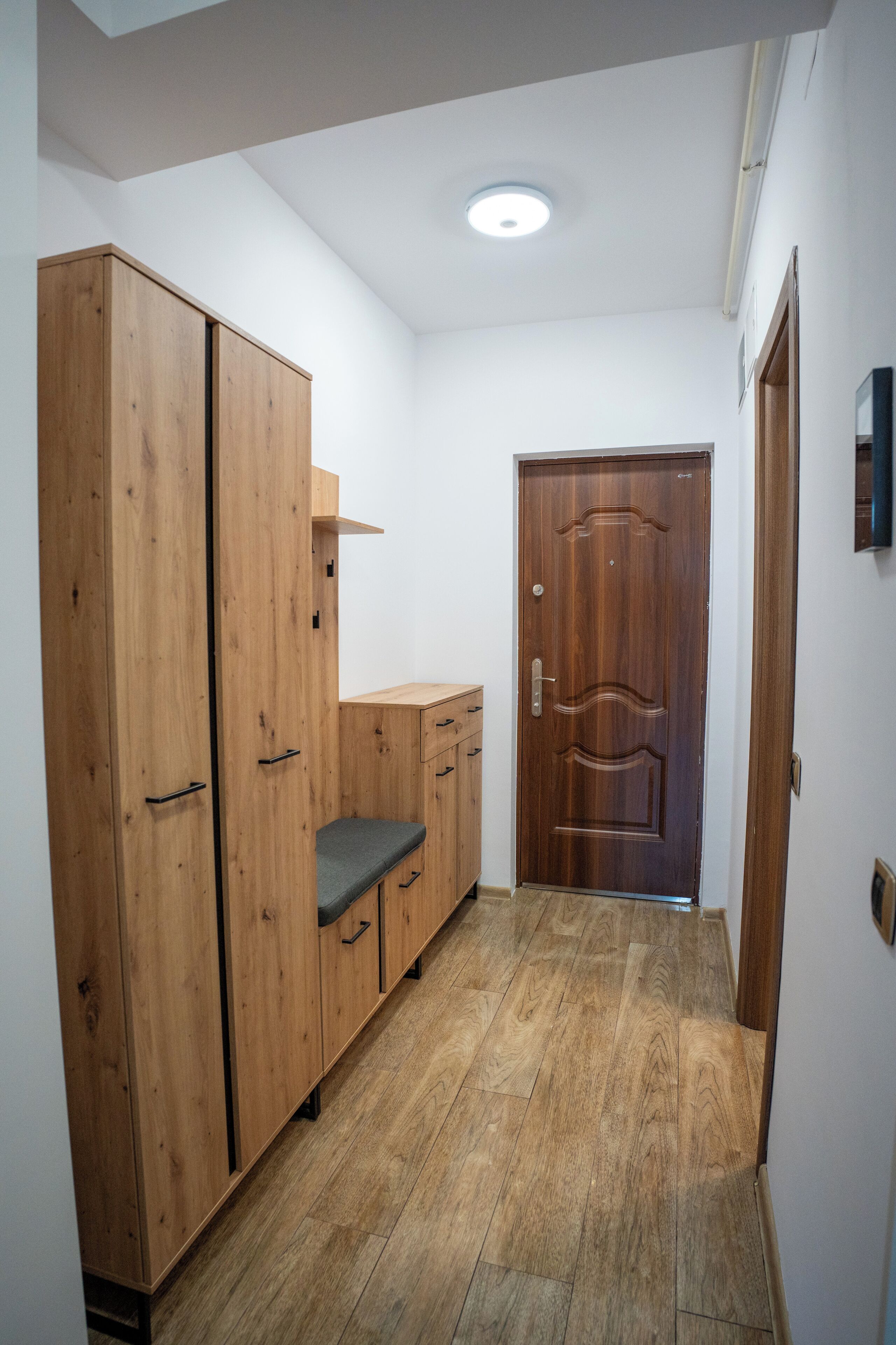 Un couloir avec un plancher en bois, une armoire, un banc et une porte.