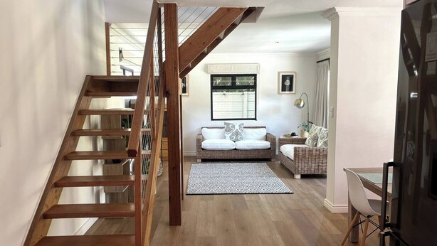 Un interior modern amb una escala de fusta, seients per a sofà, una zona de menjador i una cuina.