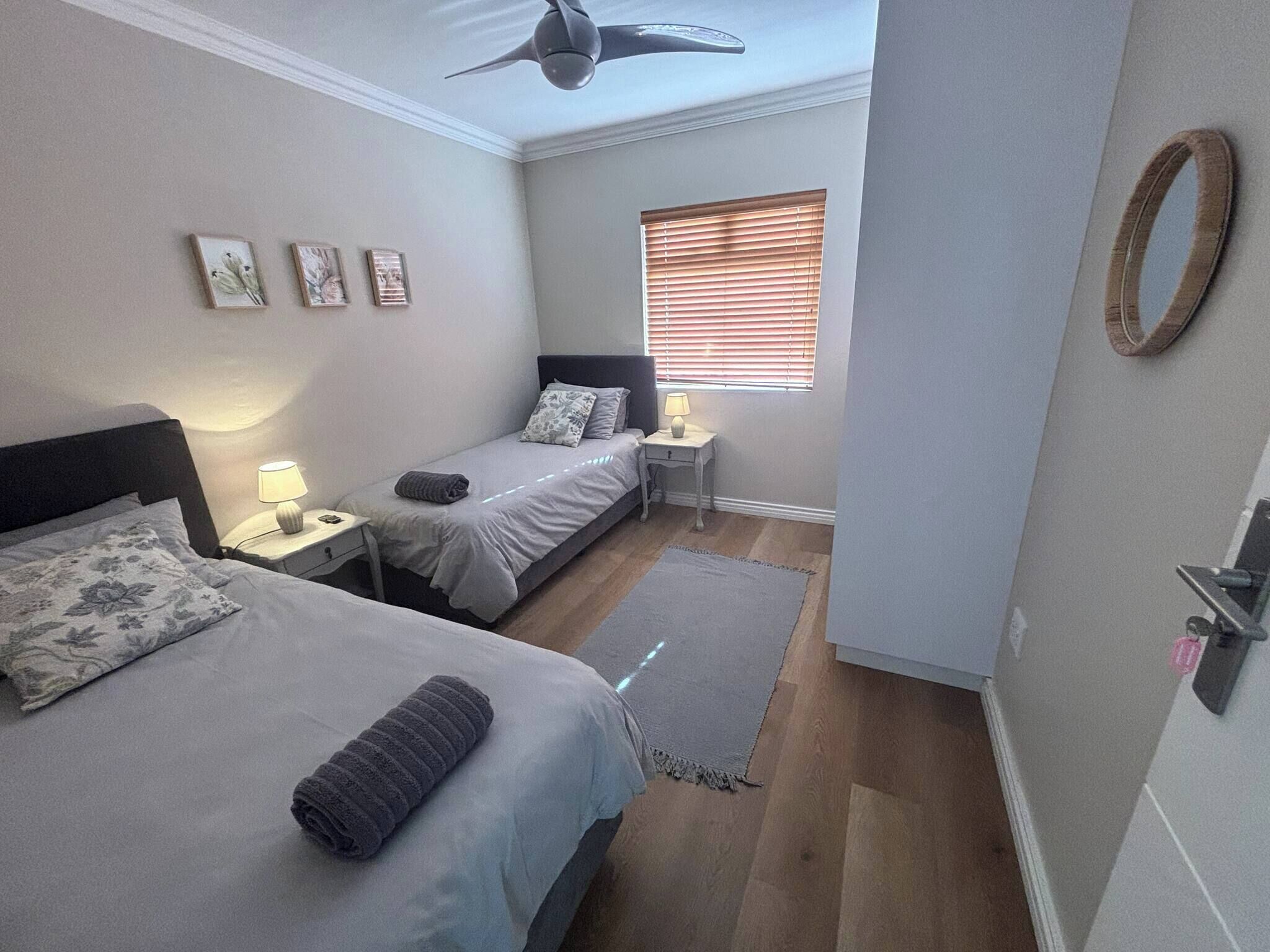 Quarto com duas camas, ventilador de teto, janela com persianas, mesas de cabeceira com luminárias e um tapete.