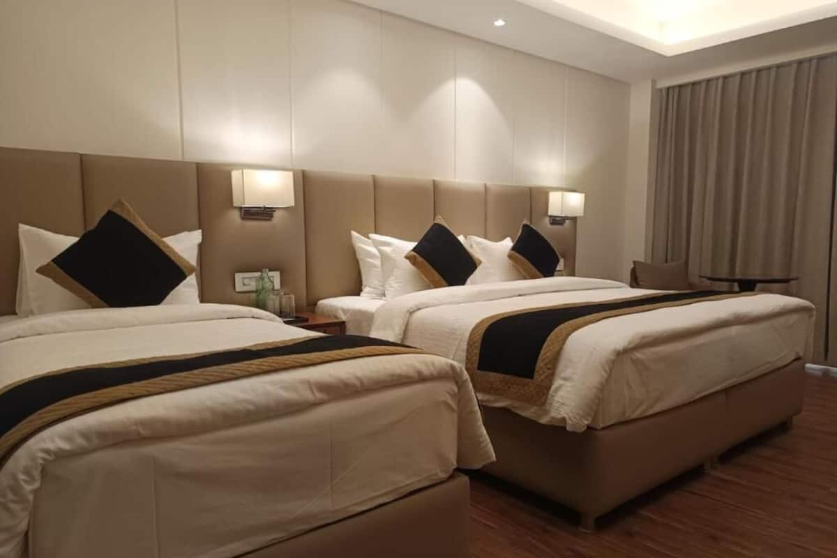 Habitación de hotel con dos camas, una mesita de noche, una lámpara y vistas al exterior.