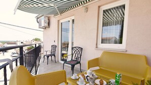 Een balkon met gele stoelen, een tafel met kopjes, een theepot en een pak melk.