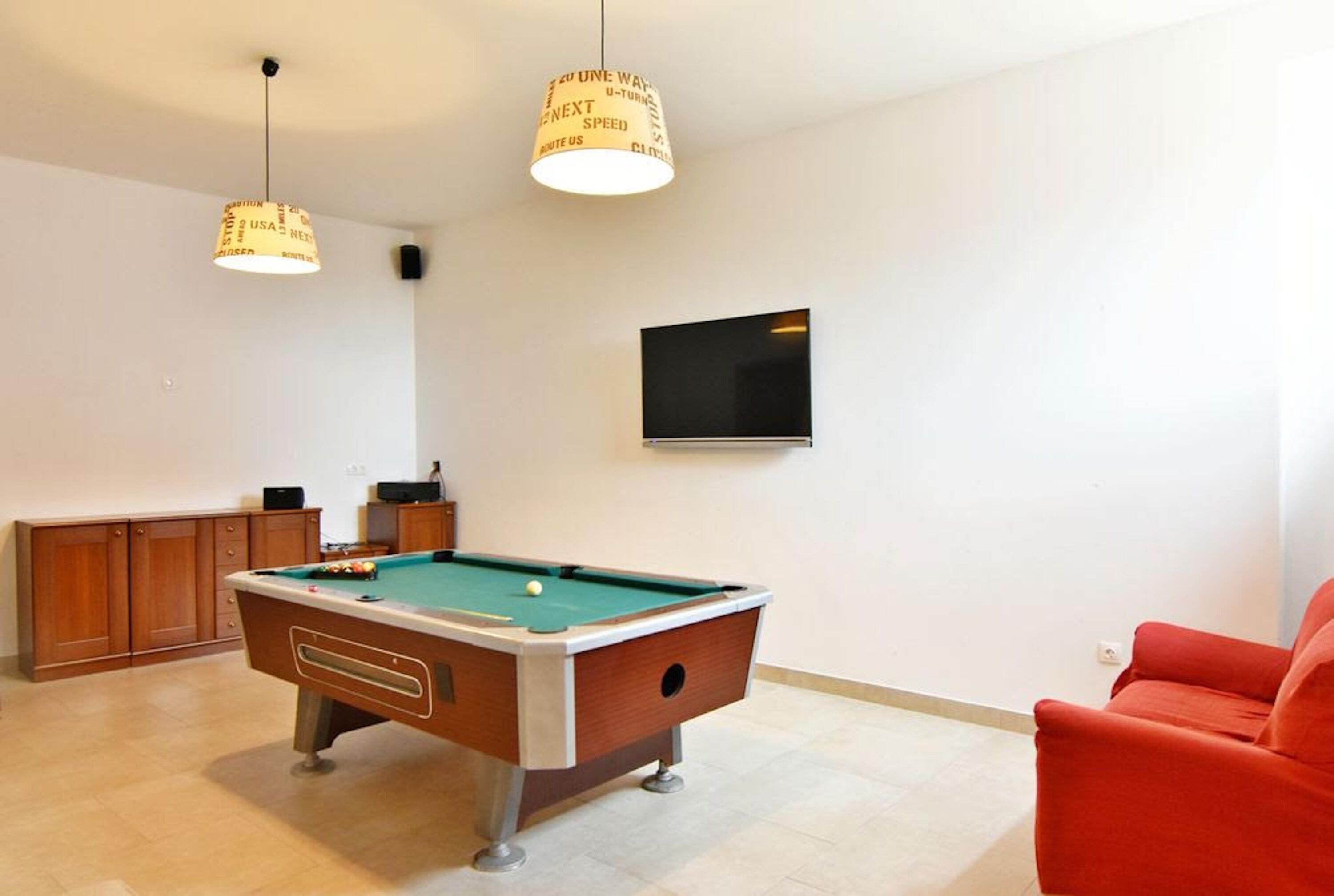 Une table de billard avec un queue de billard, une chaise rouge et un téléviseur accroché au mur.