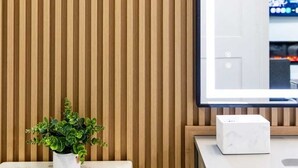 Ein Badezimmer mit einer Wand aus Holzlamellen, einem weißen Waschbecken, einer Topfpflanze und einem Spiegel.
