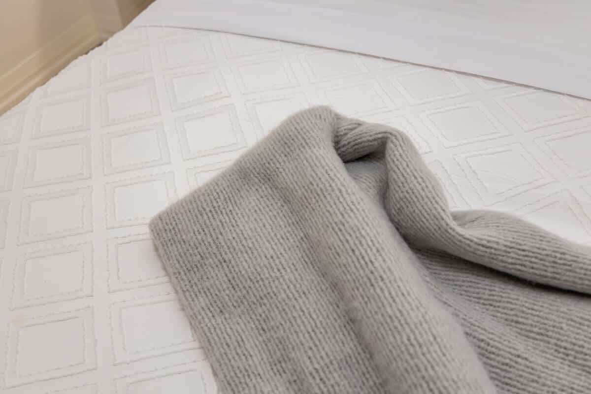 Una cama con un colchón blanco texturizado y una manta gris doblada.