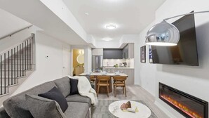 Una sala de estar moderna con un sofá gris, una mesa de centro redonda, una chimenea y un comedor con una cocina al fondo.