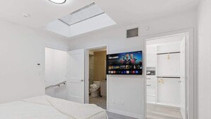 Un dormitorio con una cama, un televisor montado en la pared y un tragaluz.