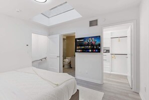 Ein Schlafzimmer mit einem Bett, einem an der Wand befestigten Fernseher und einem Oberlicht.