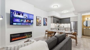 Un salon moderne doté d’un téléviseur à écran plat, d’une cheminée, d’un canapé, d’un coin repas, d’une cuisine et d’un grand miroir.