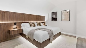 Une chambre à coucher moderne avec une tête de lit en bois, un grand lit, des tables de chevet et deux tableaux encadrés accrochés au mur.