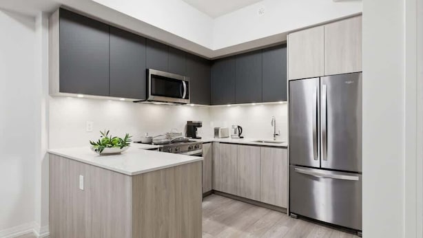 Une cuisine moderne dotée d’un îlot central, d’un four à micro-ondes encastré, d’un réfrigérateur en acier inoxydable et de meubles de rangement en bois.