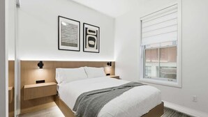 Un dormitorio con cama, mesitas de noche, una ventana y una obra de arte en la pared.