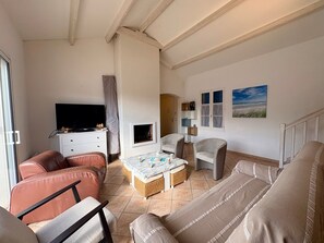 Ein Wohnzimmer mit Fernseher, Sitzgelegenheiten, einem kleinen Tisch und einem Fenster mit Blick.