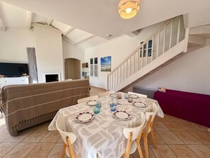 Ein Essbereich mit Tisch für vier Personen, einer Couch, einer Treppe und einem Fernseher im Hintergrund.