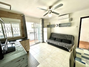 A living room with a sofa, a ceiling fan, a window with a view, a refrigerator, and a TV. - Lodging in Miami Platja - 2 guests (Miami Playa)