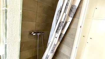 Een douche met een wit gordijn met een zwart patroon, een handdouche en betegelde wanden.