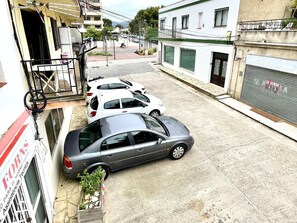 A narrow street with parked cars, a building with a closed shutter, and a sign indicating a sale. - Lodging in Miami Platja - 2 guests (Miami Playa)