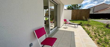 Un patio exterior moderno con puerta de vidrio, una silla roja y una tumbona.