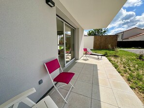 Eine moderne Terrasse im Freien mit Glastür, einem roten Stuhl und einer Sonnenliege.
