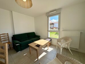Ein Wohnzimmer mit einem grünen Sofa, einem Holztisch, Korbstühlen und einem Fenster mit Blick, sowie einer Heizung.