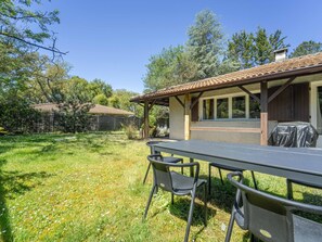 An outdoor patio with a table and chairs, a covered grill, and a house with a tiled roof and wooden beams. - Cosy house between forest and beach - 6 guests (Lit-et-Mixe)
