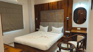 Habitación de hotel con cama, cabecero de madera, espejo redondo, mesita de noche y una silla.