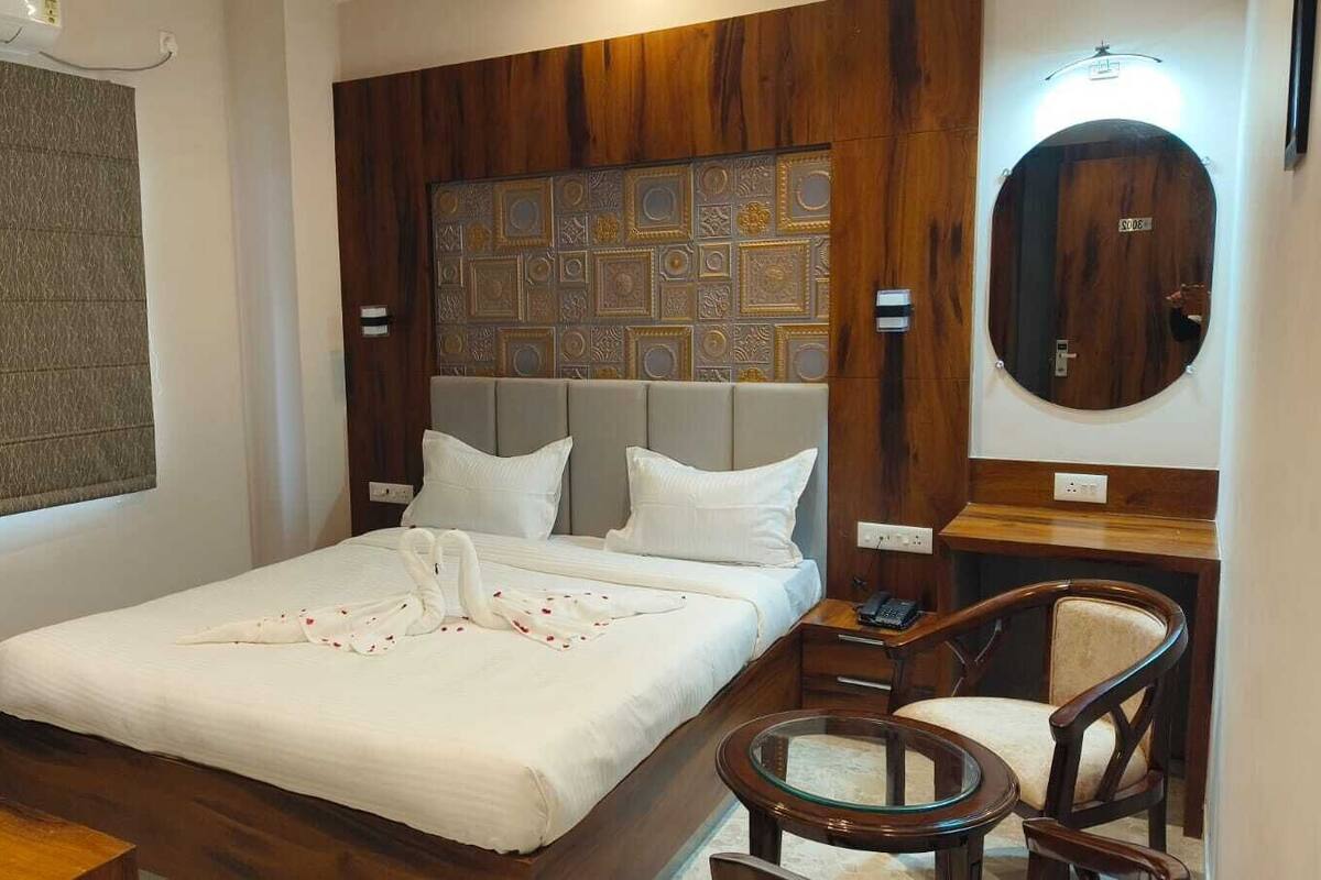 A hotel room with a bed, a wooden headboard, a round mirror, a bedside table, and a chair.